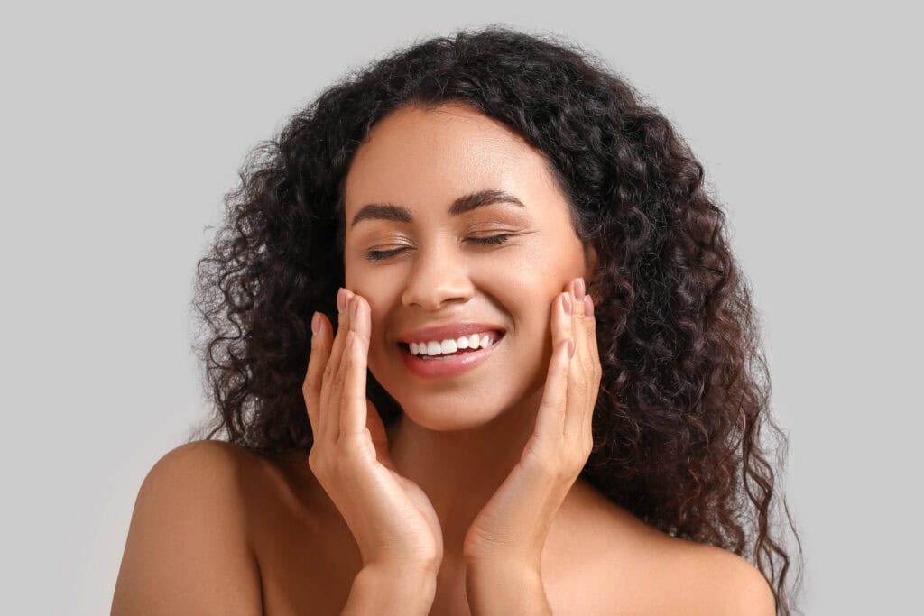Beautiful young happy African-American woman with healthy skin on grey background
